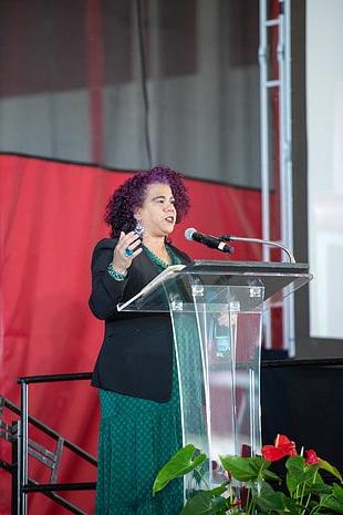 A woman speaks at a podium, delivering remarks to an audience.
